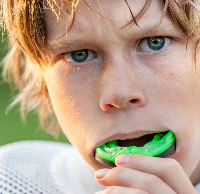 Young boy placing green athletic mouthguard into his mouth