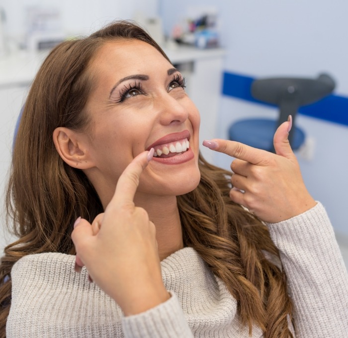 Young woman in dental chair pointing to her smile