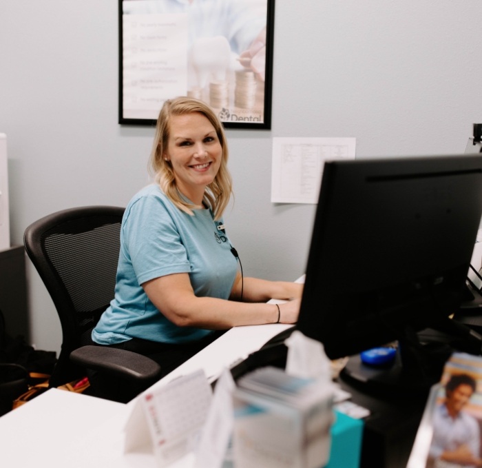 Dental team member smiling and sitting at desk with computer