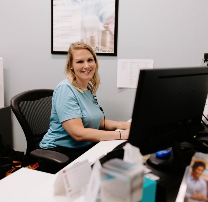 Smiling dental team member sitting at desk with computer