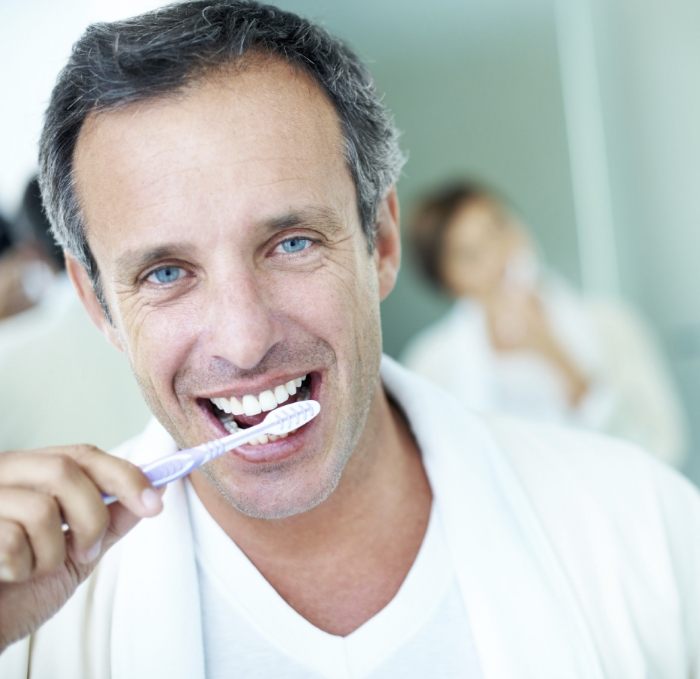 Man smiling while brushing his teeth