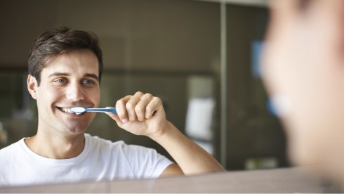 Young man brushing his teeth in front of bathroom mirror