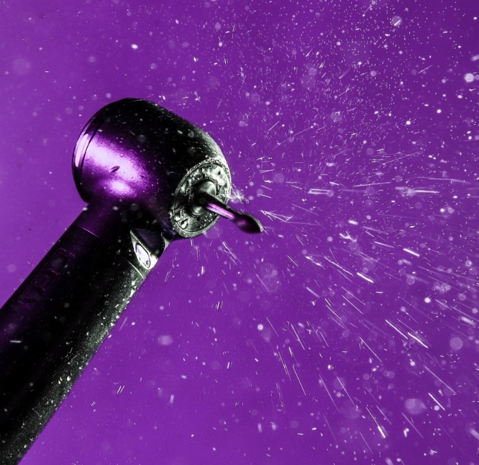 Air abrasion dental instrument spraying air in front of purple background