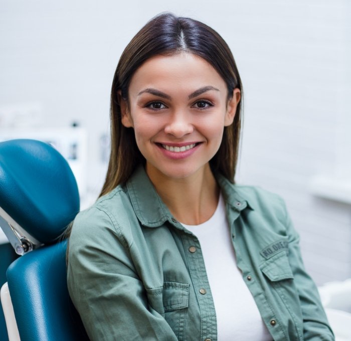 Young woman in green jacket smiling in dental chair