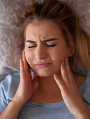 Woman rubbing her aching jaw in bed