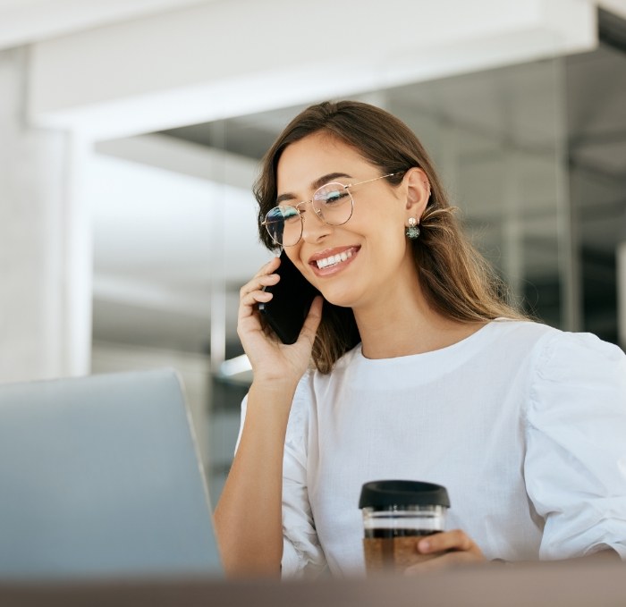 Smiling woman talking on phone while sitting at desk with laptop