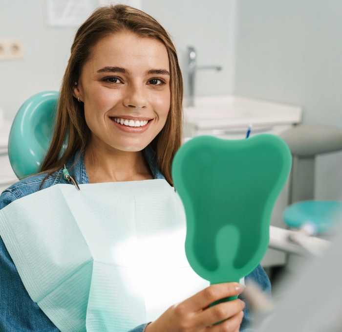 Smiling young woman in dental chair holding mirror