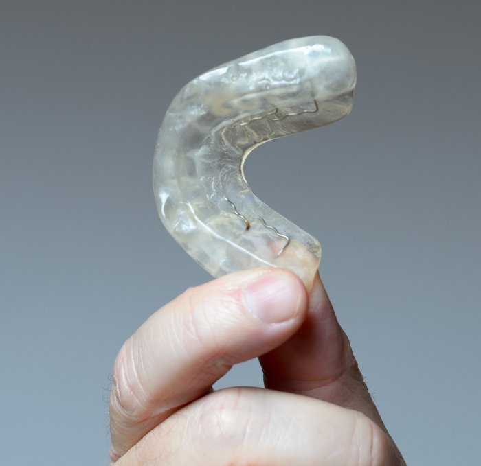 Hand holding a white nightguard for bruxism