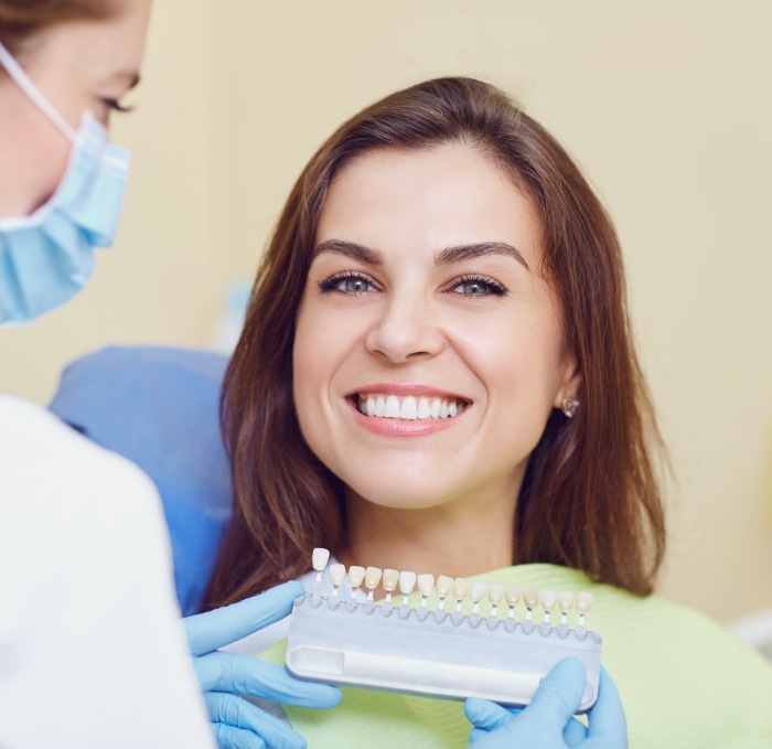 Dental patient smiling while dentist holds shade guide up to her smile