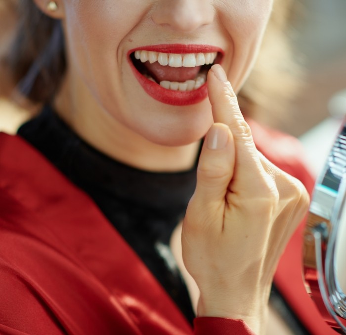 Woman with red lipstick looking at her teeth in mirror