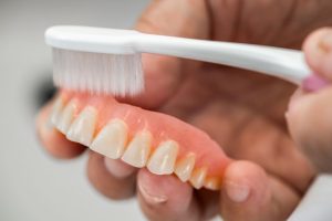 Close-up of hands cleaning denture with soft brush