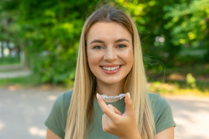 Woman in green shirt holding an Invisalign aligner